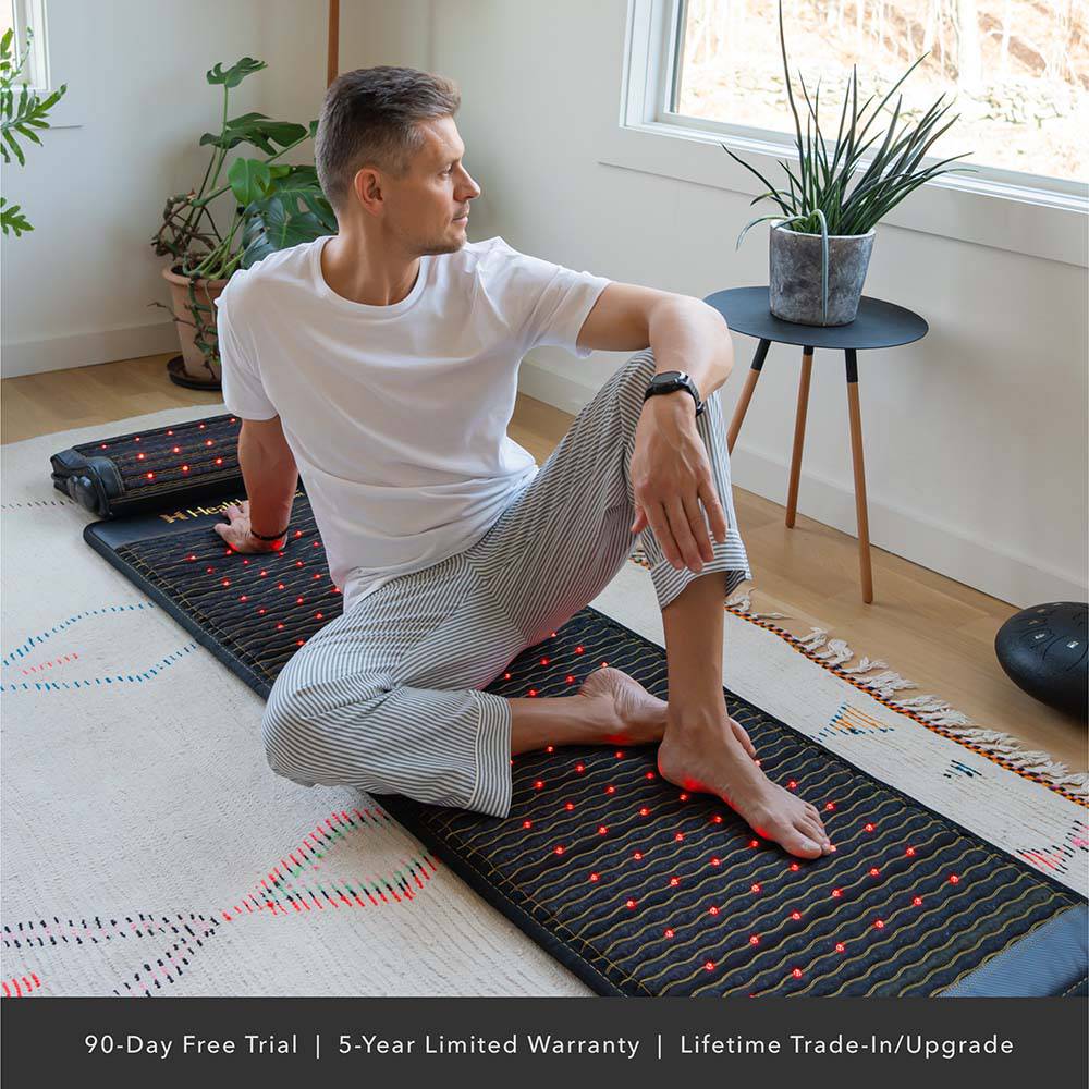 Man using Jet Mat – A man sits on a Jet PEMF mat in a bright room for relaxation
