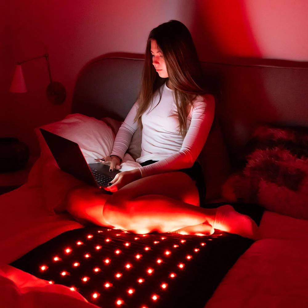 Woman with Jet Mat – A woman using a Jet PEMF mat in a dimly lit room with red light