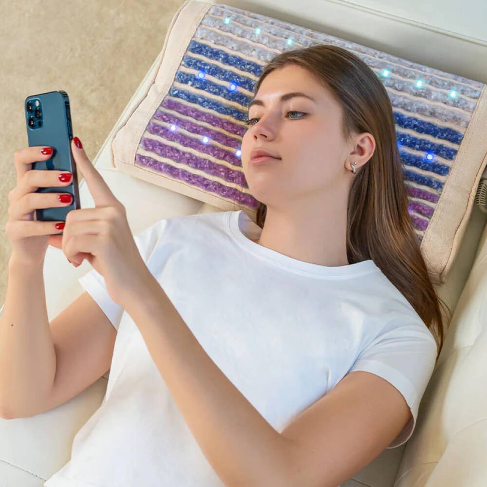 Woman lying on a couch using the Rainbow Chakra Heated Pillow for support