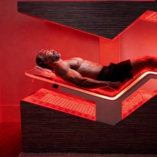 Man lying on the wellness therapy bed beneath an overhead canopy while surrounded by illuminated red light panels.