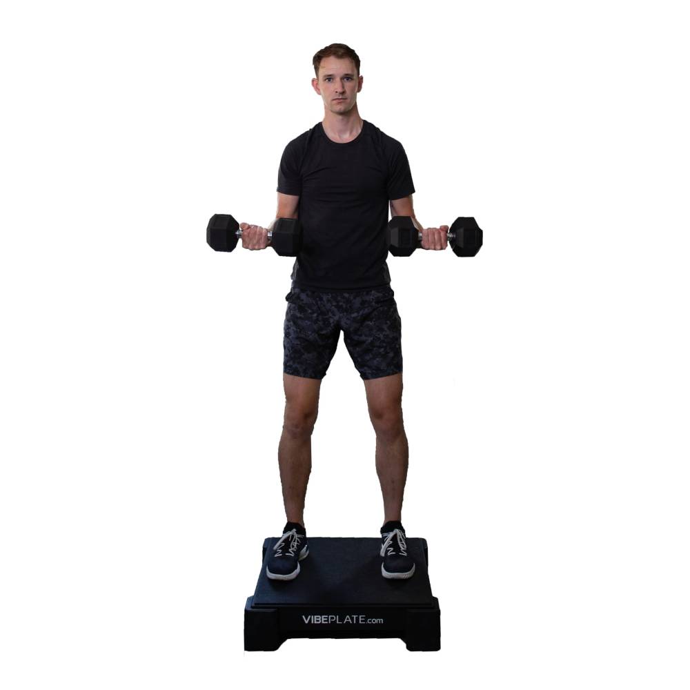 User performing dumbbell curls on the VibePlate 2424 vibration platform