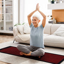 Woman in a seated yoga pose on the BioMol red light therapy mat at home