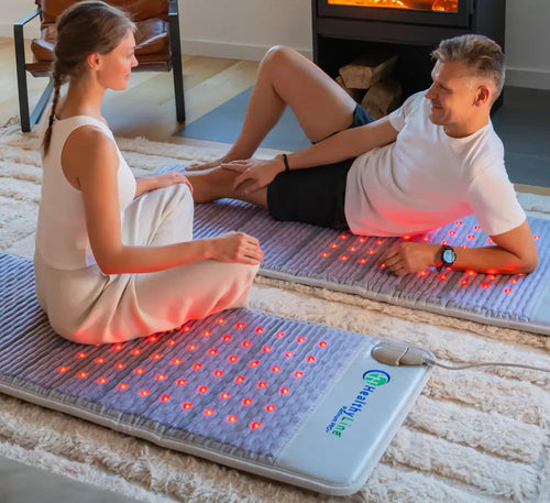 Two people sitting on the floor on a HealthyLine Platinum PEMF mat with its red photon lights glowing