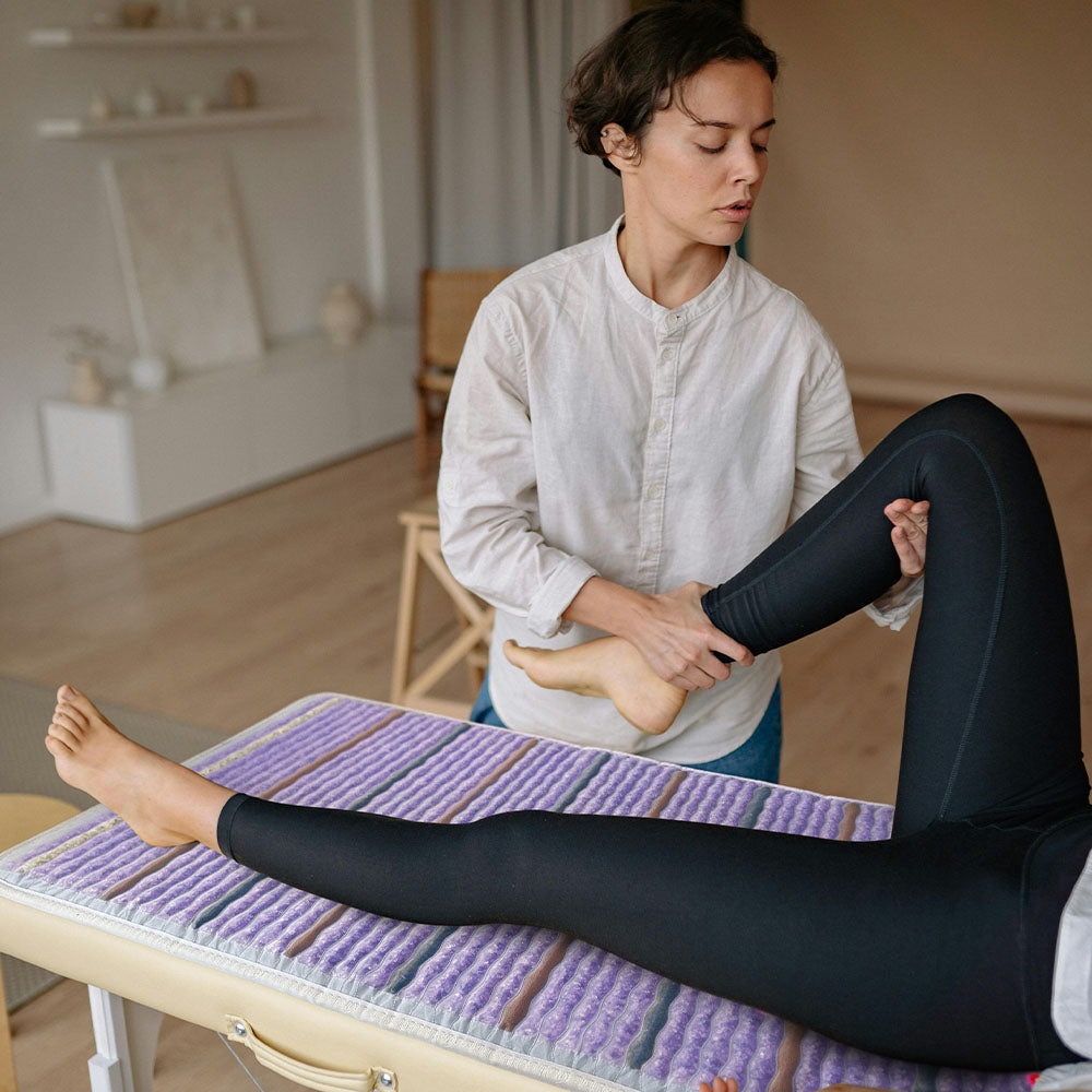 Person with a bent leg resting on a HealthyLine Platinum PEMF mat placed on a massage table