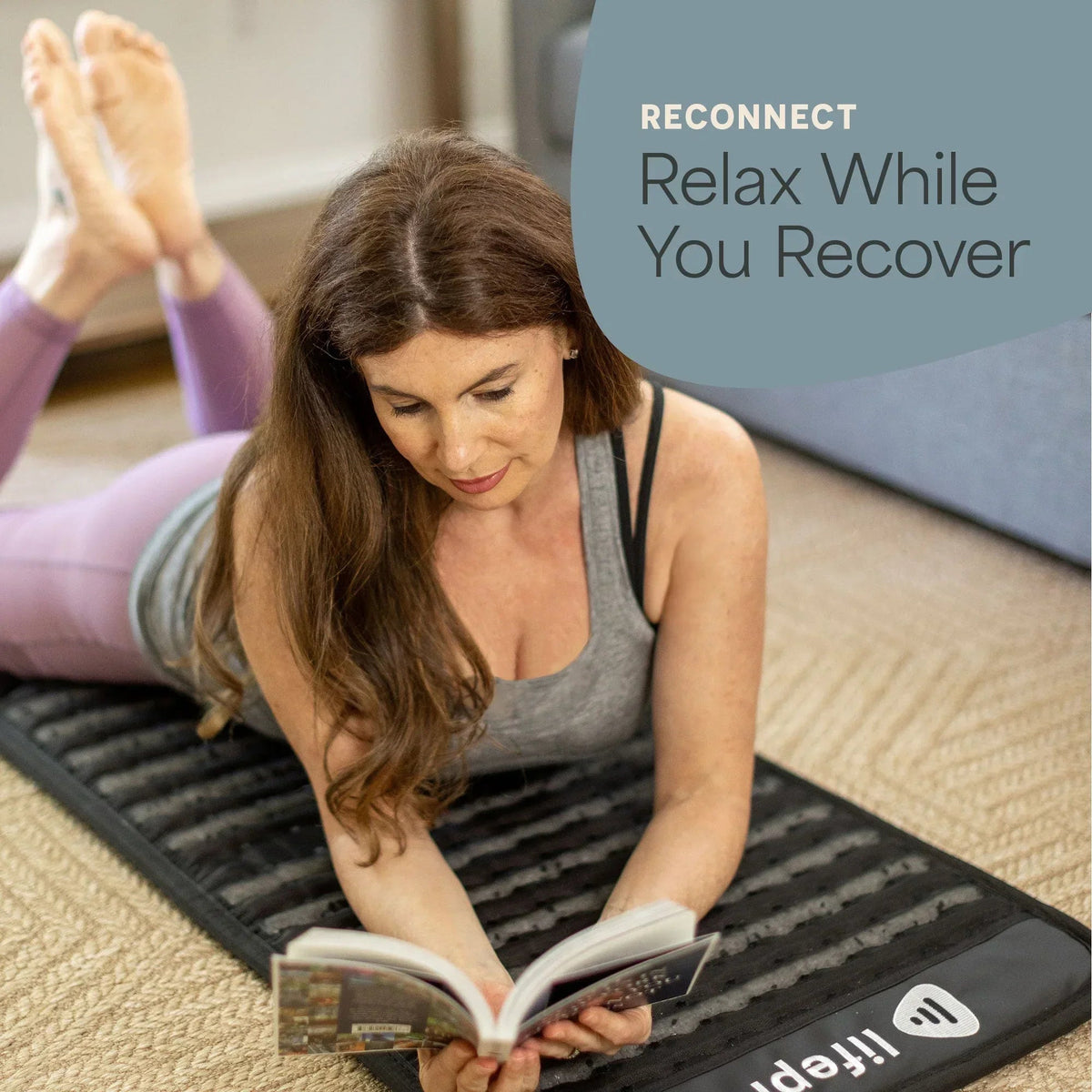 Woman relaxing on her stomach reading a book on the Lifepro InfraZen PEMF mat