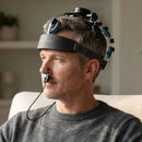 A man wearing a Vielight Neuro headset and intranasal applicator while focused on work at his laptop in a home office setting, demonstrating the device's portability.