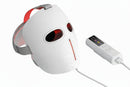 White facial mask with red lights and a remote control on a white background.