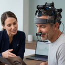 A male patient wearing the Neuro Pro 2 headset during a clinical consultation with a specialist reviewing a product brochure.