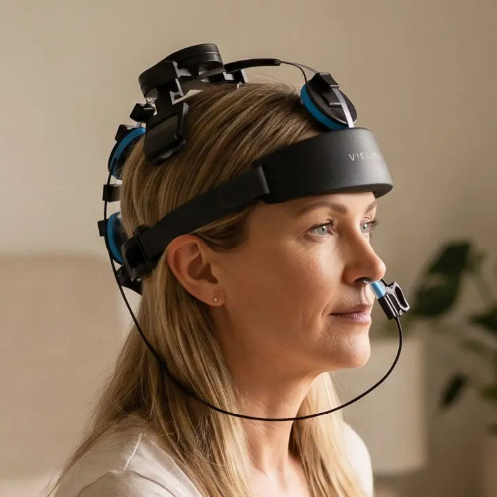 A woman sitting comfortably on a couch wearing the Vielight Neuro brain stimulation device, showcasing a hands-free wellness session at home.
